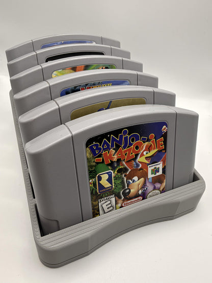 Gray six-slot N64 cartridge holder displaying six Nintendo 64 games, viewed from the front at a three-quarter angle.