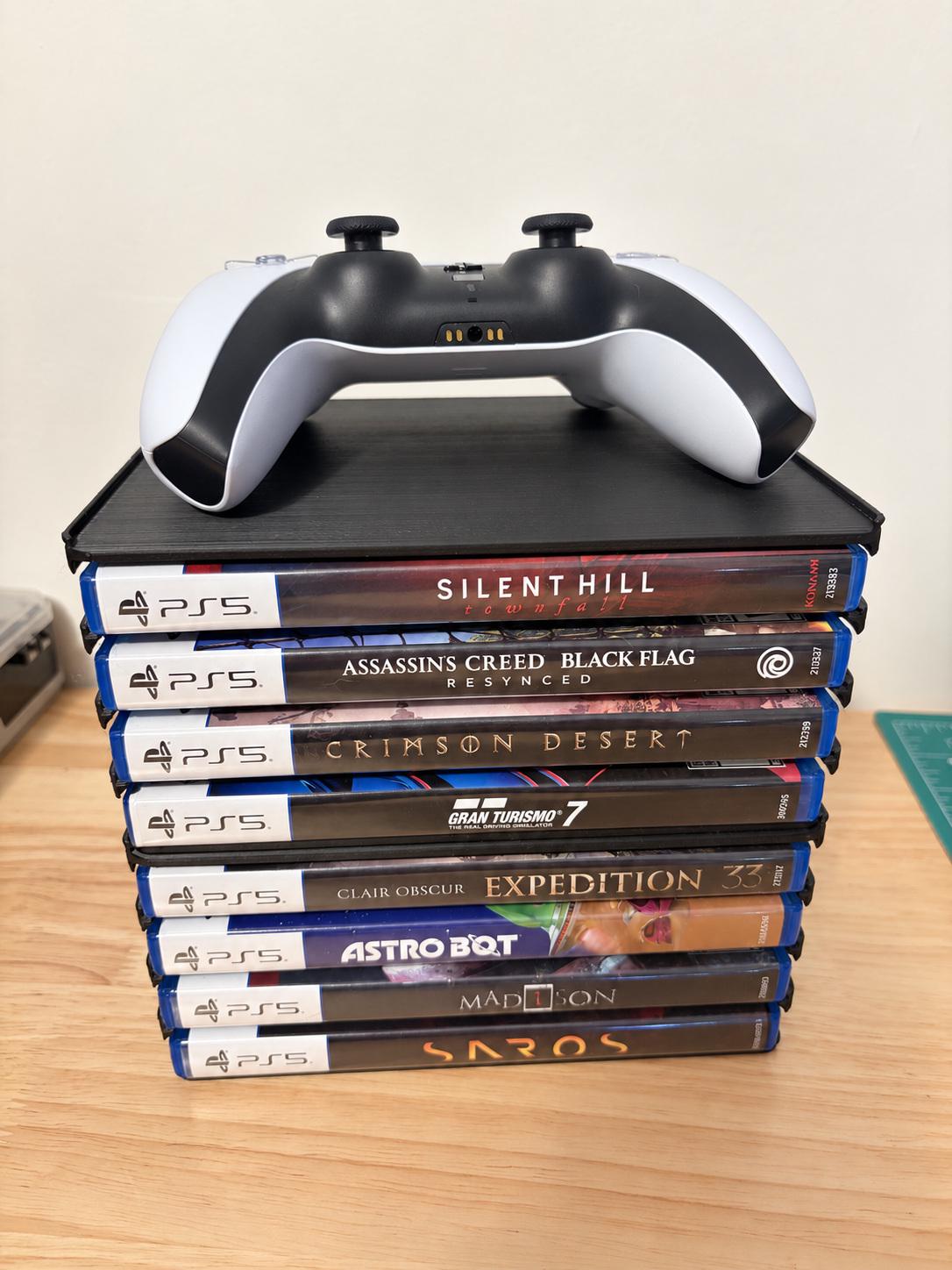 Two black holders with eight PS5 cases on a desk and a controller used as a photo prop; holder pack only.