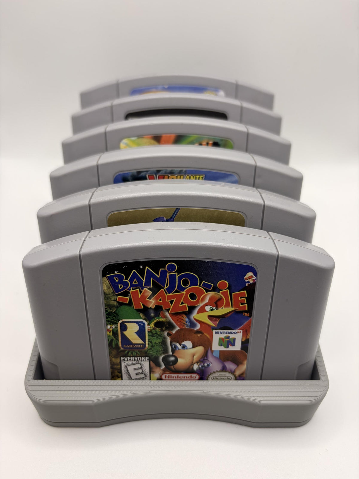 Front view of the gray N64 display holder filled with six game cartridges on a plain background.